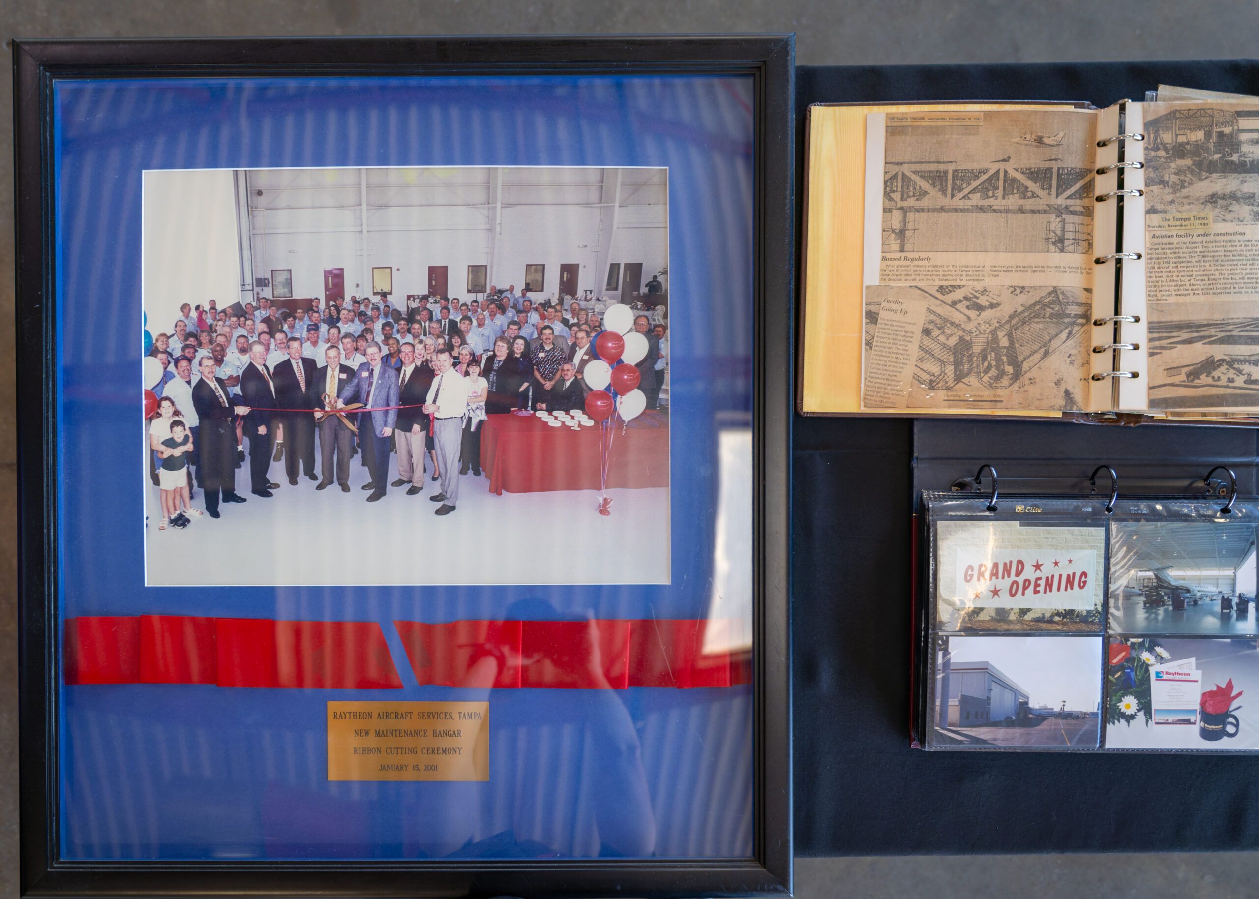 Framed photograph of a ribbon-cutting ceremony alongside historical newspaper clippings and grand opening memorabilia documenting the Tampa service centre's history
