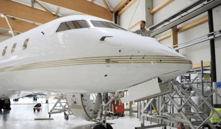 Photograph of a white Bombardier Global 5000 business jet parked on a tarmac apron with its airstair door open, shown in side profile against a clear background.