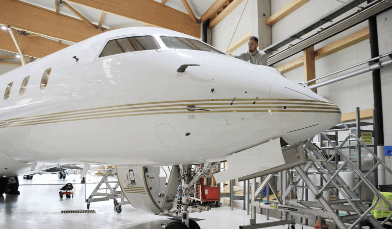 AMAC Aerospace completes Bombardier maintenance and refurbishment projects Photograph of a white Bombardier Global 5000 business jet parked on a tarmac apron with its airstair door open, shown in side profile against a clear background.