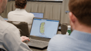 Two engineers viewing a 3D digital model of an aircraft component on a laptop screen during a design review meeting