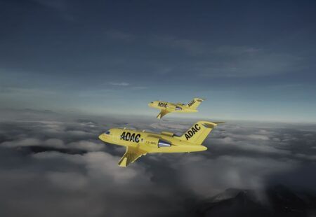 Two yellow ADAC aircraft flying in formation above clouds