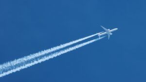 Jet airplane flying overhead in clear blue sky diagonally with condensation trail