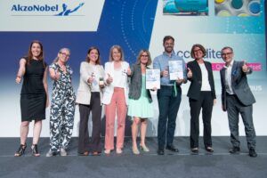 AkzoNobel team celebrates on stage with Airbus representatives at Airbus accreditation awards ceremony, giving thumbs up and holding certificates