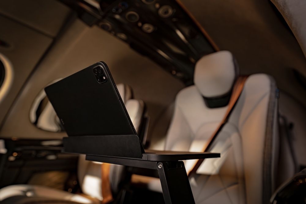 A tablet propped on a tray table deployed from the cabin sidewall of the G3 Vision Jet, with cream leather seats visible in the background.
