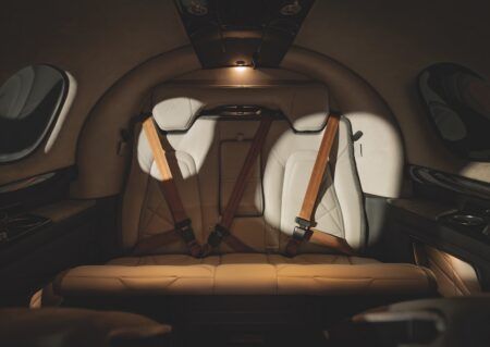 Frontal view of the G3 Vision Jet's rear bench seat in cream leather, showing harness straps and overhead lighting.