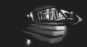 Black ACH140 helicopter mockup on a staged podium with illuminated steps, cabin interior visible through the open door showing rows of white seats, dramatic black background with two spotlights either side.