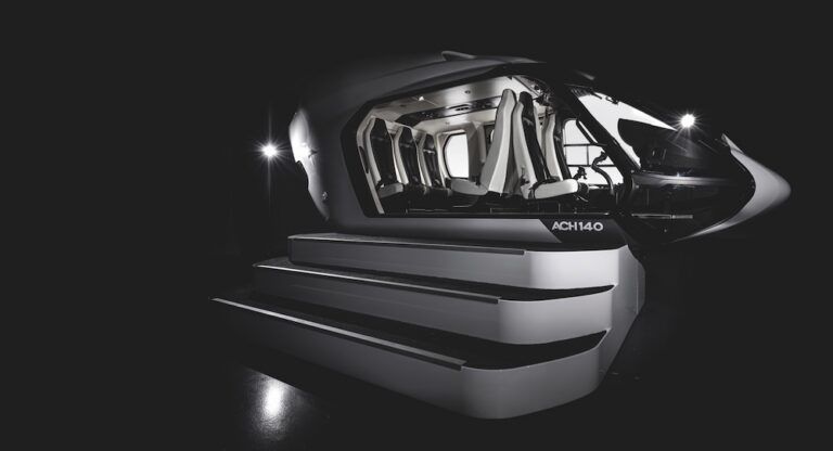 Black ACH140 helicopter mockup on a staged podium with illuminated steps, cabin interior visible through the open door showing rows of white seats, dramatic black background with two spotlights either side.