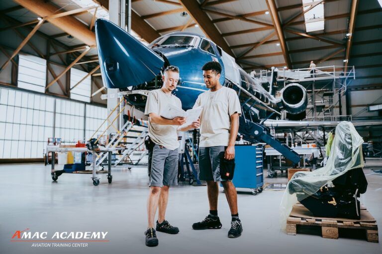 Aircraft maintenance training programme launched by AMAC Two people in AMAC uniforms reviewing documents in front of an aircraft undergoing maintenance inside a hangar, with the AMAC Academy Aviation Training Center logo visible.