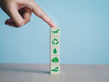 A stack of wooden blocks printed with green sustainability icons, including an aircraft, a recycling symbol and a CO2 cloud