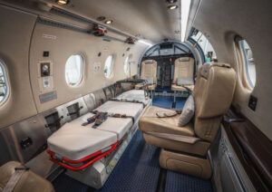 The interior of a small aircraft configured for air medical use, with a patient stretcher on the left, a leather seat on the right and medical equipment panels along the cabin wall.