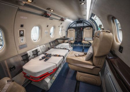 The interior of a small aircraft configured for air medical use, with a patient stretcher on the left, a leather seat on the right and medical equipment panels along the cabin wall.