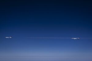 Two business jets flying in formation against a deep blue sky at high altitude