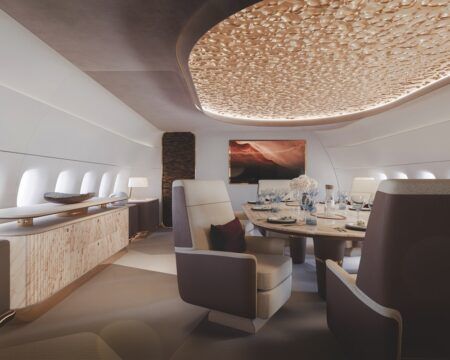 FEATURE: Lightweighting at Jet Aviation Business jet cabin interior featuring a circular dining suite with cream leather swivel chairs, a textured gold dimpled ceiling panel with concealed lighting, and a wood-veneer credenza along the sidewall.