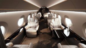 Forward cabin of a Gulfstream G700 business jet featuring cream leather seats, dark wood cabinetry, gold accents, oval windows and a high-gloss black table.