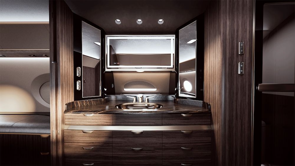 Aircraft lavatory vanity area with dark marble countertop, sink, illuminated mirror and rich wood-grain cabinetry.