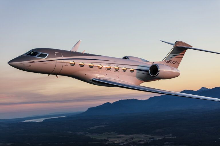 A Gulfstream G650ER business jet in flight at dusk above mountains
