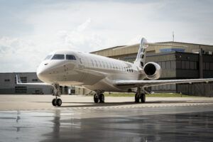 A white Bombardier Global 8000 business jet parked on an apron in front of a hangar