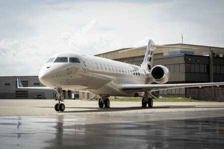 A white Bombardier Global 8000 business jet parked on an apron in front of a hangar