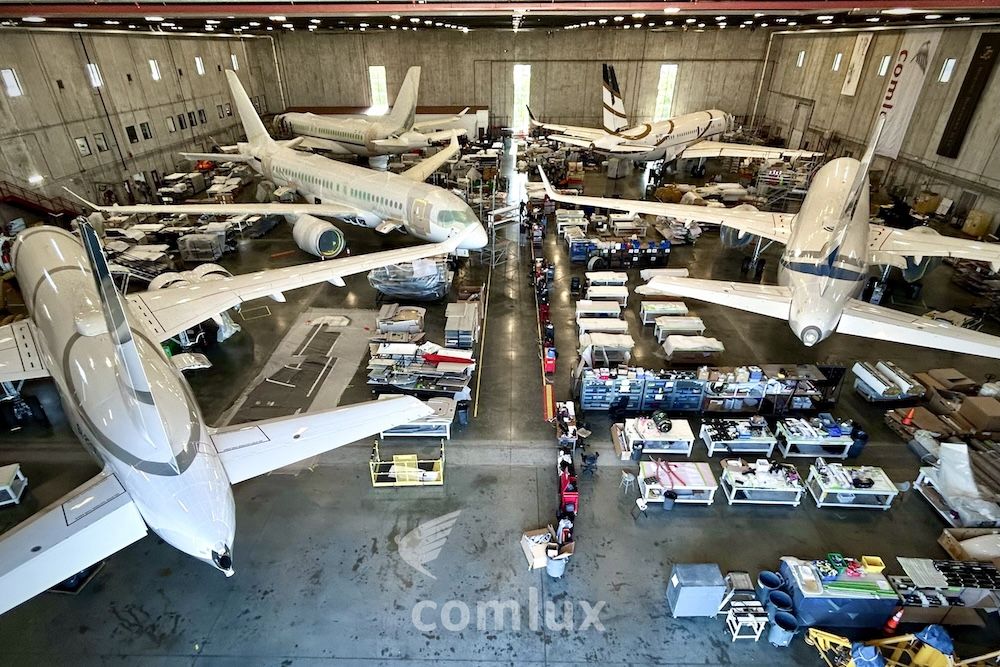 Aerial view inside Comlux America’s completions hangar showing several business jets undergoing work, surrounded by workstations, tooling and materials on the hangar floor.