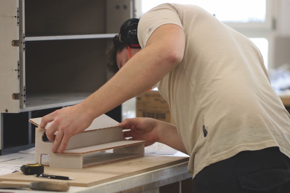 A technician wearing ear defenders assembles a lightweight honeycomb sandwich panel structure on a workbench.