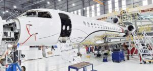 Aircraft in a maintenance hangar with open nose section and cabin door, surrounded by access platforms and ground equipment