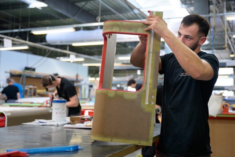 FEATURE: Lightweighting in business jet cabin completions A technician in a JCB Aero workshop holds up a red-edged composite cabin monument panel, inspecting the honeycomb core and bonded surface finish.