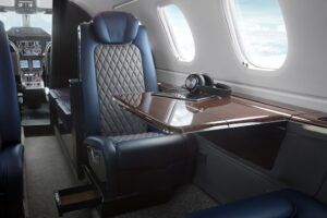 Phenom 300EV cabin interior showing a blue and grey leather seat and wood veneered table with headphones