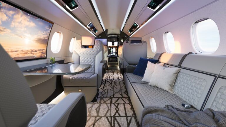 Praetor 600E cabin interior at sunset, featuring the curved Smart Window displaying an external sky view, a fold-out table, patterned carpet and cushioned divan.