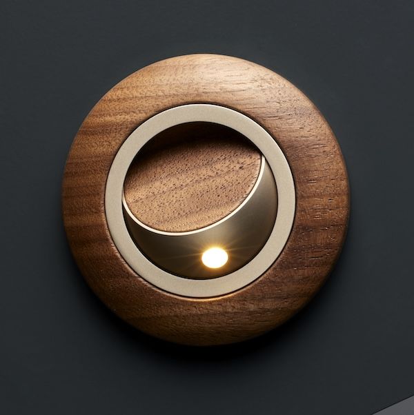 Circular Schott Opal Terra reading light with a wood surround, illuminated against a dark background