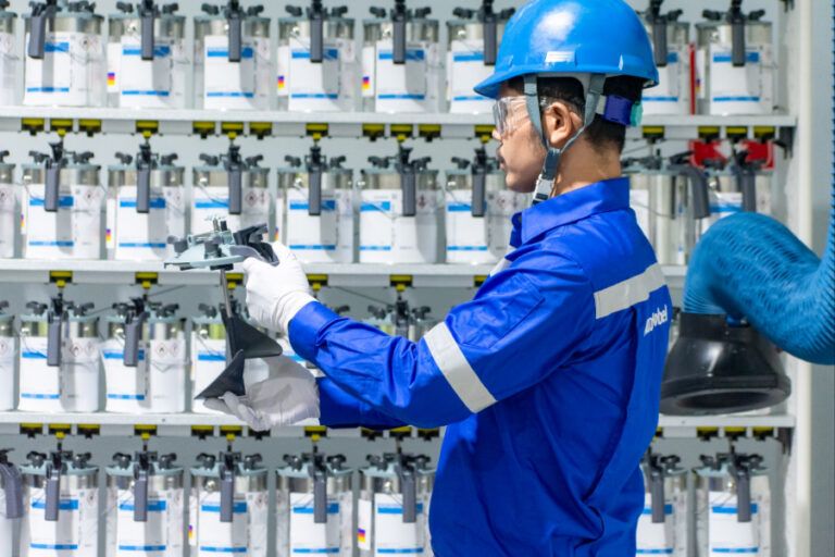 Technician handling coating equipment in front of stacked shelves.