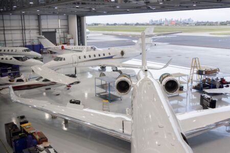 Part 145 approval for Textron Aviation service centres in Australia Wide interior view of an aircraft maintenance hangar with several business jets, hangar doors open to a runway beyond
