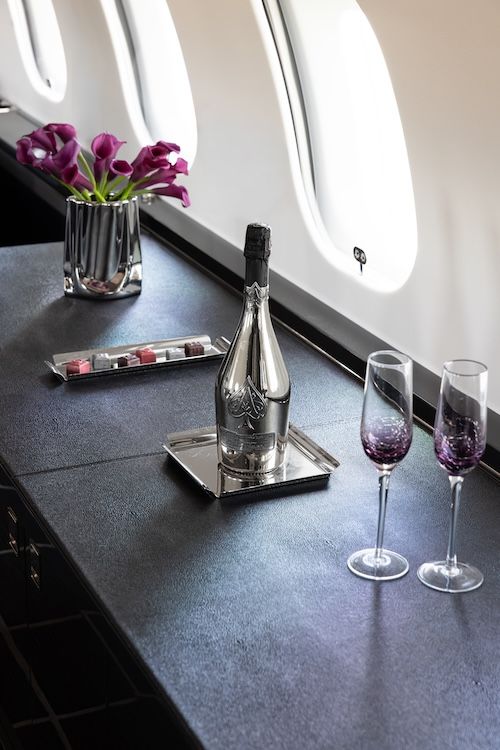 Champagne, chocolates and flowers on top of a side credenza on board private jet