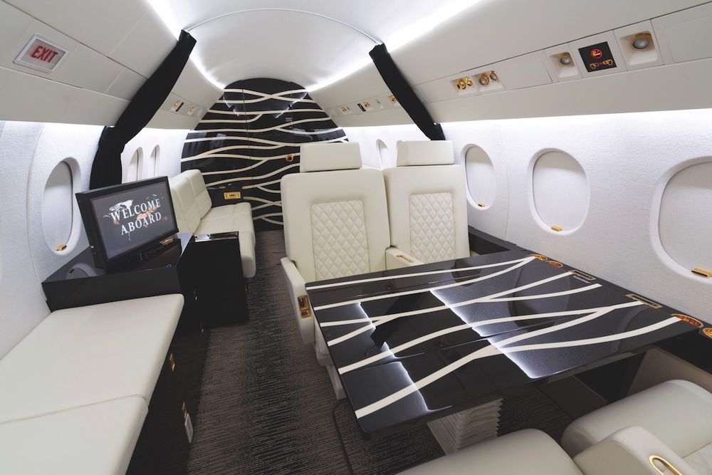 Business jet cabin with white leather seats and divan, and a high-gloss black table and bulkhead with flowing white stripes
