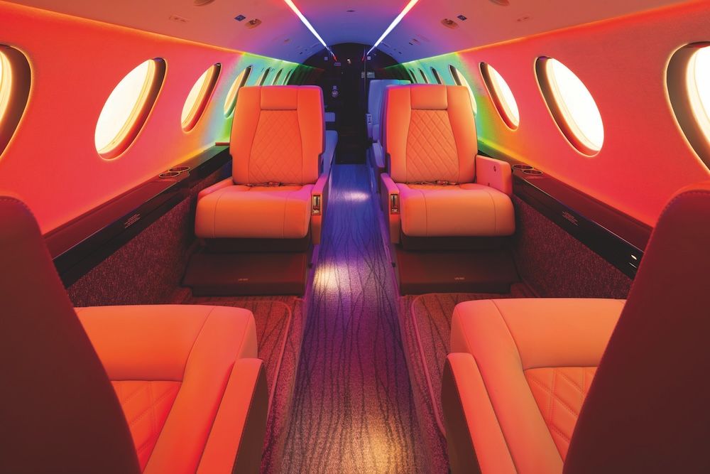 Business jet cabin with cream leather club seats washed in red, orange and green LED mood lighting along the sidewalls