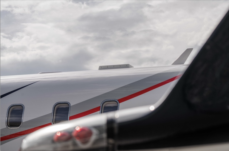 Business jet fuselage, painted white and grey with red and navy stripes, with a low-profile antenna on top
