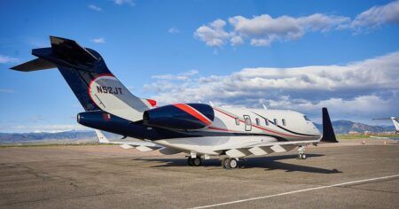A business jet with a white, navy and red livery parked on an apron, with mountains and blue sky behind