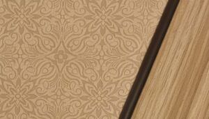 Close-up of BBJ cabinetry showing a textured leather insert with an embossed floral pattern, edged in dark leather welt cord and framed by satin-finished wood veneer