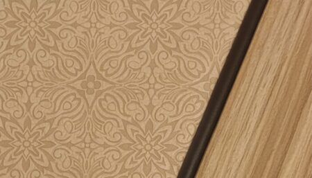 Close-up of BBJ cabinetry showing a textured leather insert with an embossed floral pattern, edged in dark leather welt cord and framed by satin-finished wood veneer