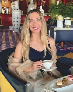 Natalie Rodríguez, smiling and holding a teacup, seated in a luxury hotel lounge with large decorative vases behind her