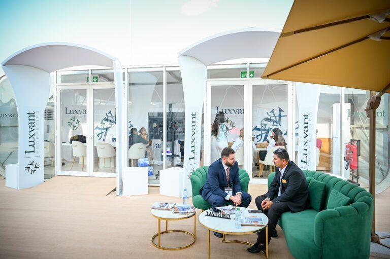 Two men talking on green sofas outside Luxvant Properties pavilion